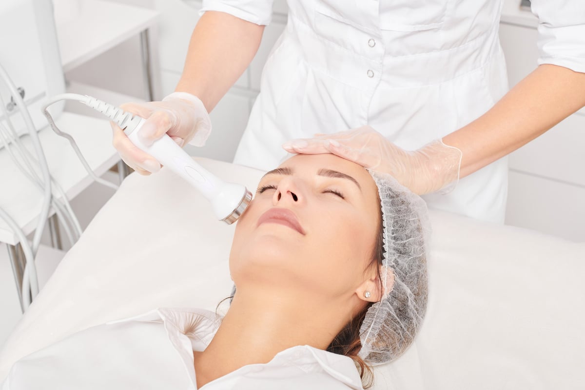 Beautician makes ultrasound skin tightening for rejuvenation woman face using phonophoresis, anti aging cosmetic procedure with in beauty spa salon