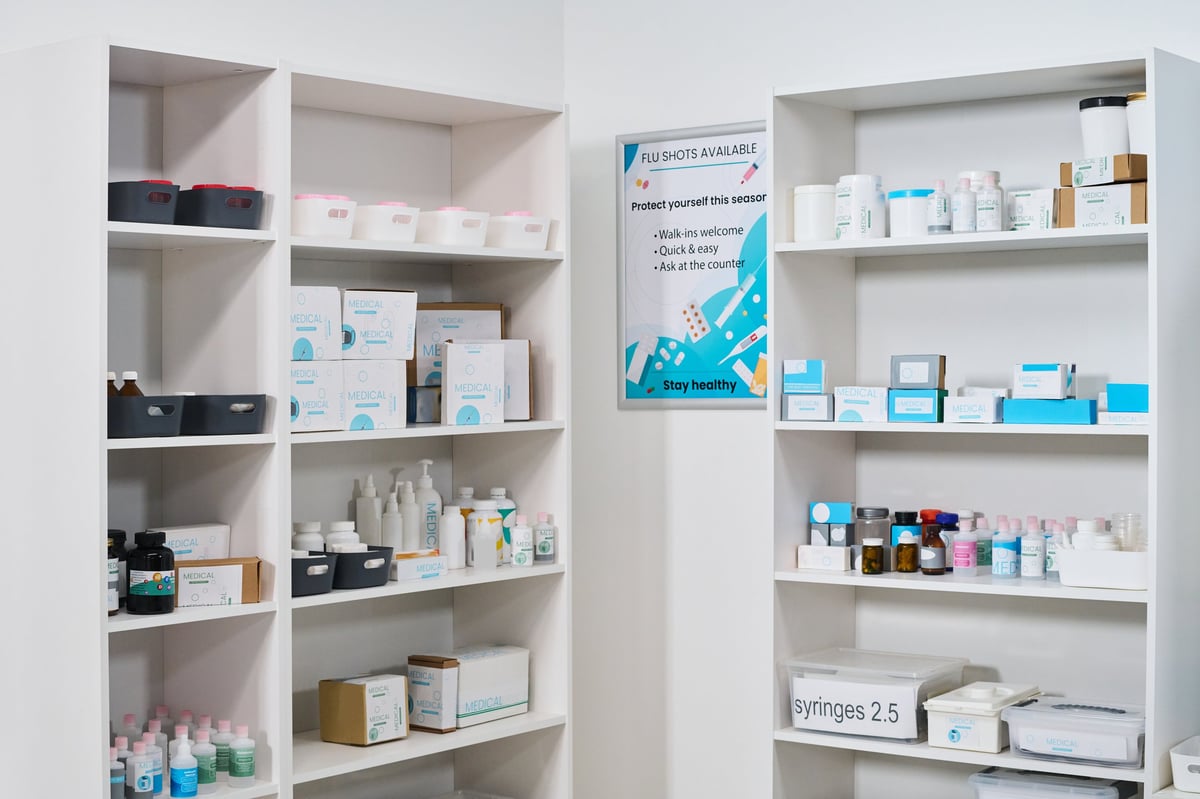Wide shot of pharmacy shelves displaying medical supplies, syringes, bottles, boxes, promoting vaccination and clinic inventory management. Ideal for healthcare retail, immunization, pharmacy services